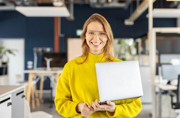 Deutschlandstipendium HS 2025 Eine Frau mit Laptop im Arm lächelt in die Kamera.