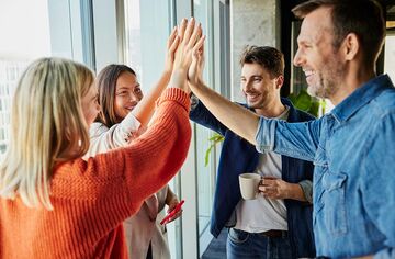 Zwei Frauen und zwei Männer stehen im Kreis und klatschen in der Mitte mit ihren Händen ab.