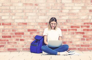 Studentin sitzend mit Laptop vor einer Wand