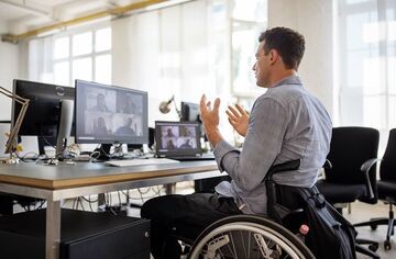 Mann im Rollstuhl vor Bildschirmen nimmt an Webinar teil und diskutiert