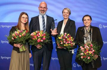 Drei Frauen und ein Mann auf einer Bühne mit Auszeichnungen in der Hand