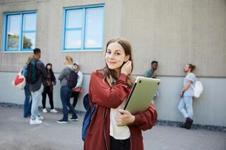 Junge Frau mit Notebook auf Schulhof, die sich die Haare hinter die Ohren macht