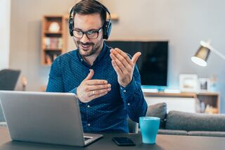Gestikulierender Mann mit Kopfhörern vor Notebook