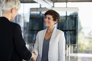 Zwei Geschäftsfrauen schütteln sich lächelnd die Hände, symbolisch für erfolgreiche Zusammenarbeit im Fernstudium.