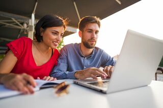 Frau und Mann an Tisch schauen gemeinsam in Laptop