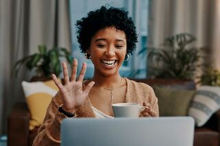 Frau, dunkelhäutig, schaut lachend in Laptop