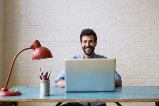 Mann sitzend an Tisch vor Notebook und Lampe
