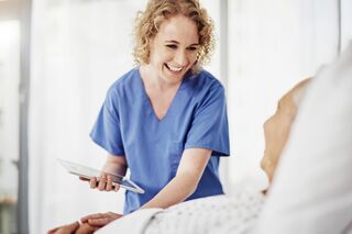 Junge Pflegerin lächelt mit Tablet in der Hand Patientin