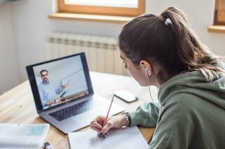 Junge Frau sitzt am Schreibtisch vor einem Computer und schreibt auf einen Block