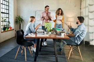 Vier junge Menschen stehen und sitzen um einen Tisch und diskutieren