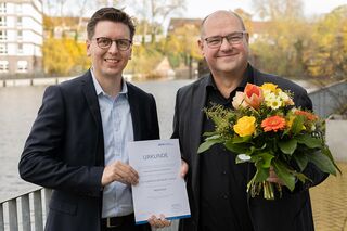 Prof. Dr. Lars Binckebanck überreicht Prof. Dr. Florian Oldenburg-Tietjen die Ernennungsurkunde und einen Blumenstrauß.