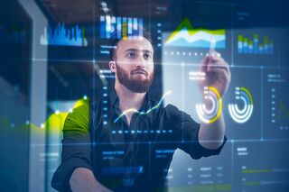 Junger Mann steht vor digitaler Wand mit eingeblendeten Schaubildern und Statistiken