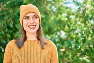 Frau mit gelber Strickmütze und Pullover lächelt und schaut schräg nach oben.