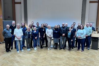 Gruppenbild mit 24 Personen in Veranstaltungsraum