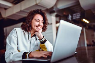 Junge Frau sitzt lächelnd an Tisch vor Notebook