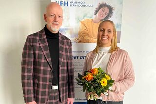 Dr. Jochen Holzkamp und Prof. Dr. Cathleen Gaede-Illig mit Blumenstrauß vor Roll-up.
