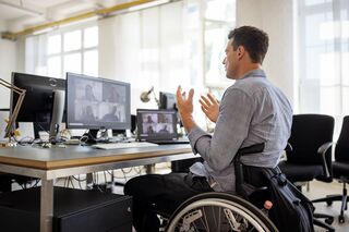 Mann im Rollstuhl vor Bildschirmen nimmt an Webinar teil und diskutiert