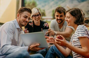 Vier Menschen sitzen lachend um einen Laptop.