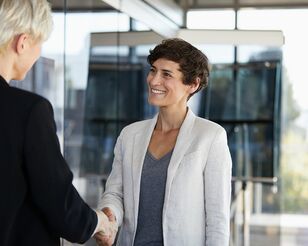 Zwei Frauen im Business-Umfeld schütteln Hände und lächeln