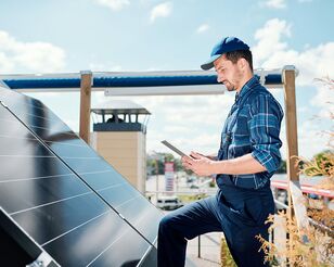 Mann in Blaumann steht auf Dach vor Solar-Panel mit Tablet in der Hand