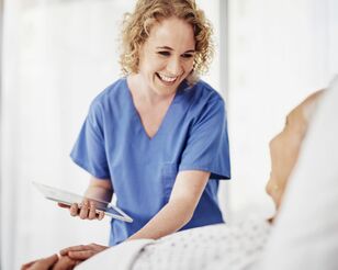 Junge Pflegerin lächelt mit Tablet in der Hand Patientin