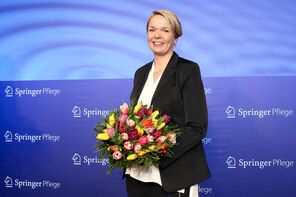 Foto: Britta Pedersen/Springer Pflege Katharina Gerkens mit Blumenstrauß vor blauem Hintergrund