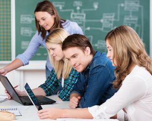 Vier junge Studierende an einem Schreibtisch auf Laptops schauend