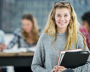 Blonde Frau mit Studienheften schaut lachend in Kamera