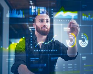 Junger Mann steht vor digitaler Wand mit eingeblendeten Schaubildern und Statistiken