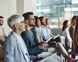 Menschen sitzen in Stuhlreihen auf einer Konferenz und hören einen Vortrag