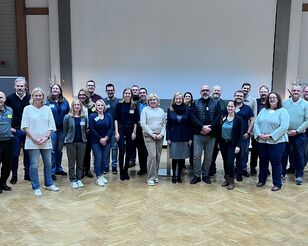 Gruppenbild mit 24 Personen in Veranstaltungsraum