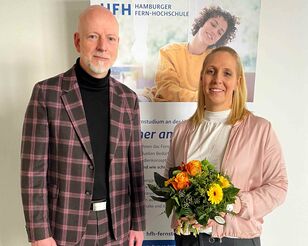 Dr. Jochen Holzkamp und Prof. Dr. Cathleen Gaede-Illig mit Blumenstrauß vor Roll-up.