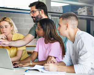 drei Studierende und ein Lehrender an einem Tisch mit Laptop