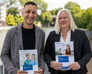 Prof. Dr. Michael Heinrich-Zehm steht links neben Prof. Dr. Eske Jung vor dem Osterbekkanal in Hamburg; beide halten je einen Studienführer der HFH in der Hand.