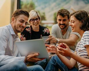 Vier Menschen sitzen lachend um einen Laptop.