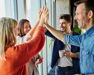Zwei Frauen und zwei Männer stehen im Kreis und klatschen in der Mitte mit ihren Händen ab.