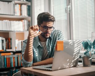 Studierender sitzt am Tisch mit Laptop und Lernmaterial, arbeitet konzentriert in heller, moderner Umgebung.