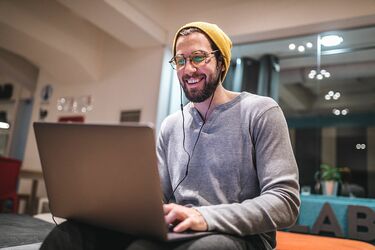 Mann mit Mütze sitzt vor Notebook und lächelt