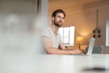 Mann sitzt am Laptop und guckt nachdenklich in die Luft