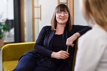 Frau unterhält sich lächelnd mit jüngerer Frau auf einem Sofa 