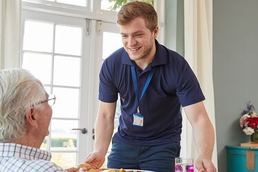 Junger Altenpfleger bringt Senioren Essen auf einem Tablet