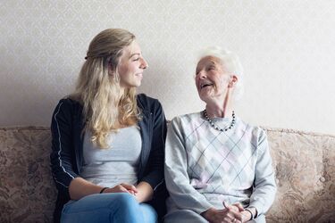 HFH Therapie- und Pflegewissenschaften Bachelor Junge Frau sitzt zusammen mit älterer Dame auf Couch und lacht herzlich