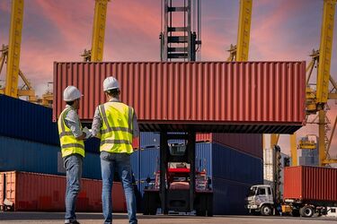 Zwei Männer in Warnwesten vor einem Containerterminal