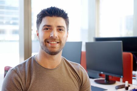 Junger Mann sitzt im Büro vor einigen Monitoren