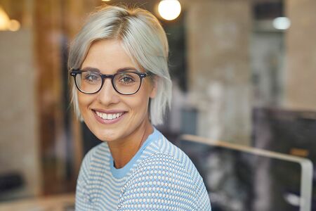 Frau mit Brille lächelt in die Kamera. Sie sitzt in einem Büro.