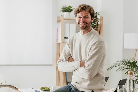Lächelnder Mann in einem hellen, modern eingerichteten Raum mit Pflanzen im Hintergrund