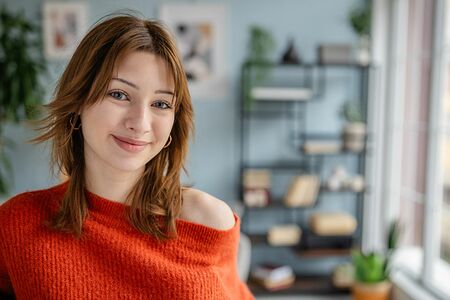 Lächelnde Frau in orangefarbenem Pullover in einem hellen Wohn- und Arbeitsraum