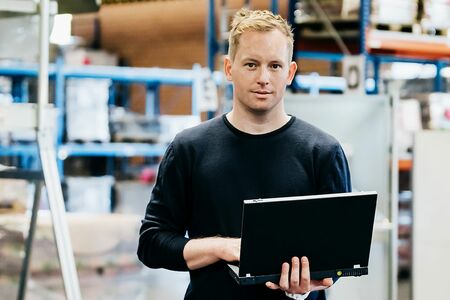 Mann steht mit Laptop in der Hand in Fabrikhalle