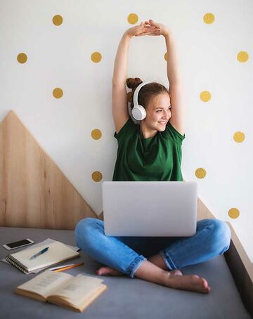 junge Frau streckt sich, vor ihr steht ihr Laptop und Studienmaterialien