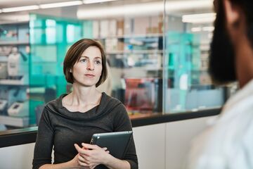 HFH Pflegemanagement Bachelor Frau steht mit IPad in der Hand und unterhält sich mit einem wissenschaftlichen Mitarbeiter